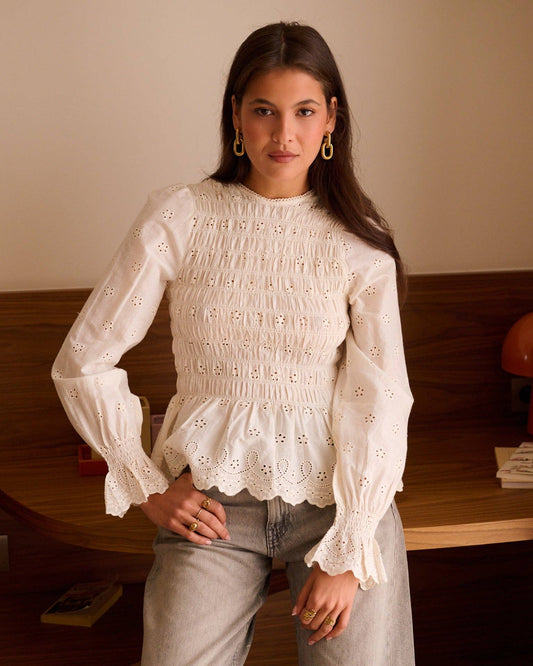 Blouse Élia écrue à broderies ajourées et buste smocké, portée avec un pantalon clair.